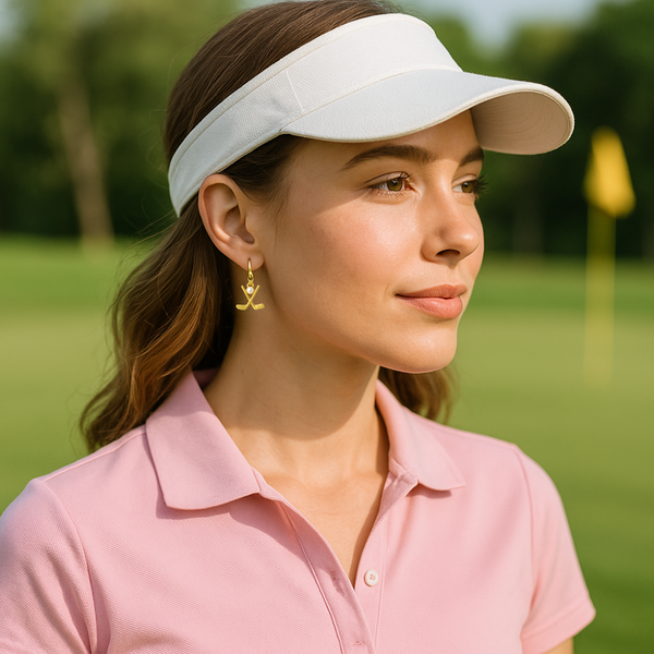 Woman wearing gold golf pearl dangle earrings and a visor on a golf course, highlighting her love for golf.
